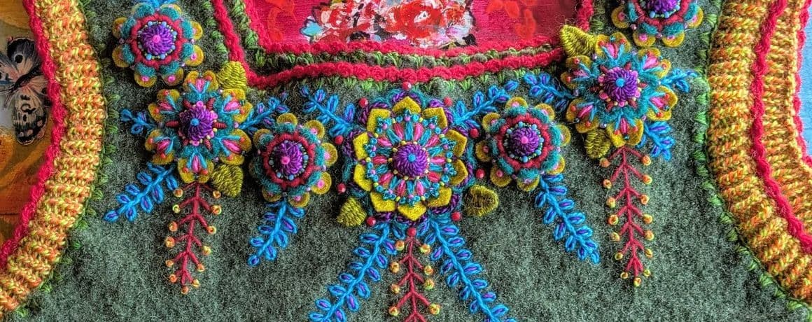 Handbesticktes  ärmelloses Oberteil aus grünem Walkloden mit bunten, handgestickten Blumen und Ranken, Arm- und Halsausschnitte sind mit orangem Garn gestrickt